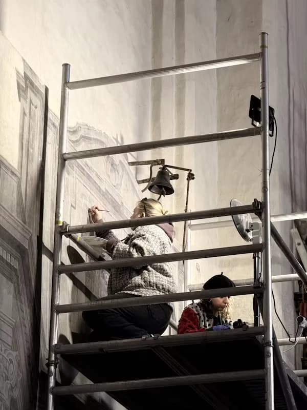 Restauradores trabajando sobre un andamio en la pared de una sala