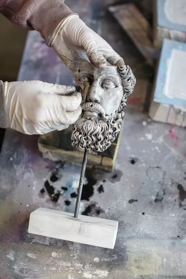 Mano enguantada retocando el busto de una escultura con barba
