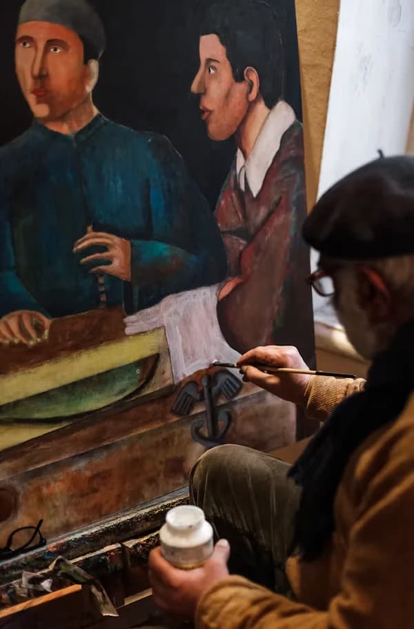 Restaurador retocando una pintura con dos figuras, con un bote de pigmento en primer plano